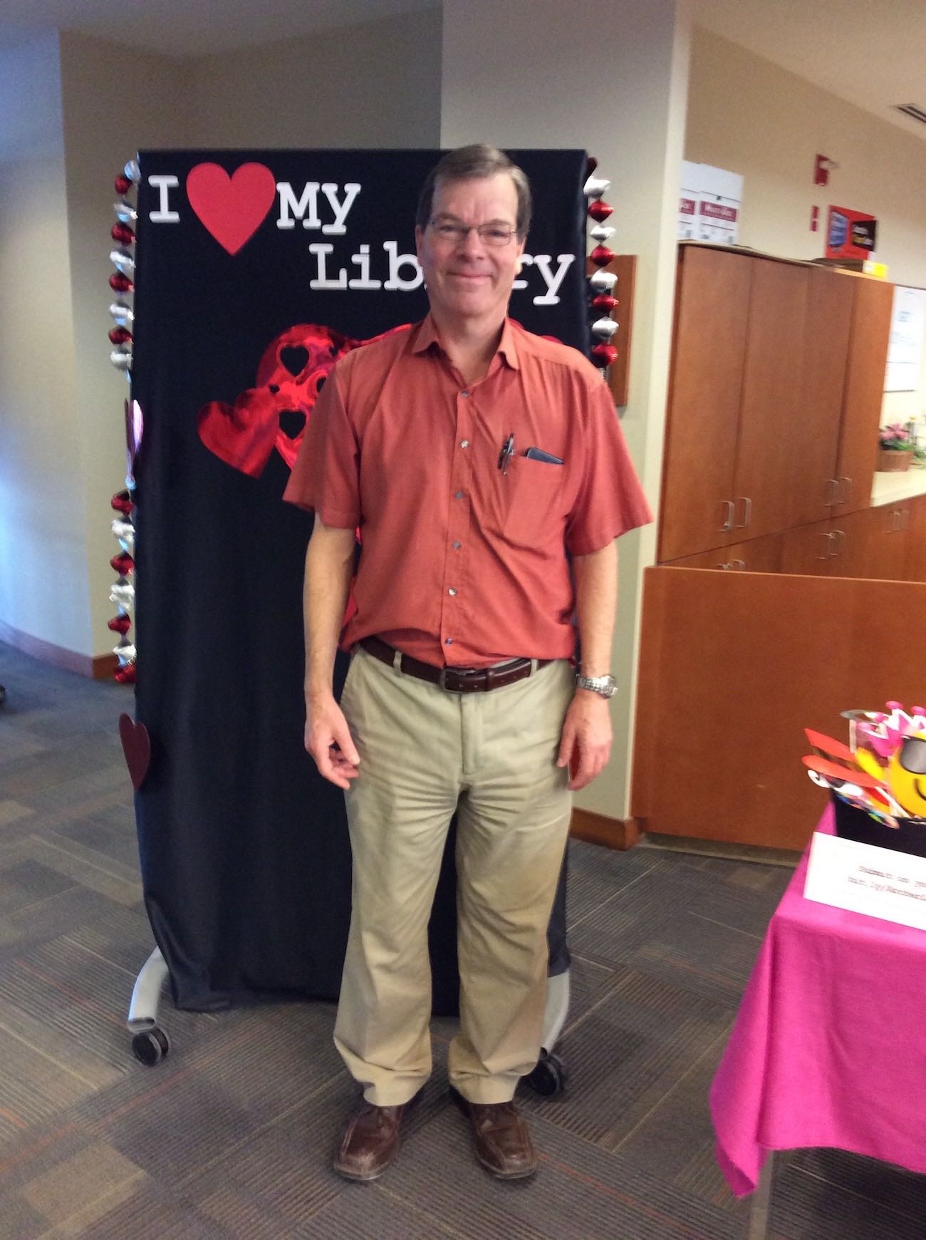Librarian Charles Phelps stands in front of the I love my library backdrop smiling